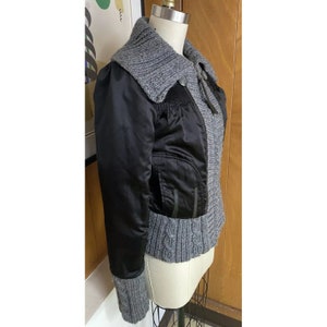 May include: A black and grey jacket with a zip fastening and a knitted collar. The jacket has a satin-like finish and a cable knit trim.