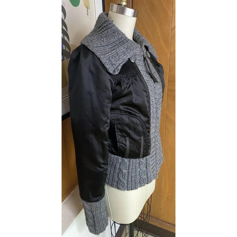May include: A black and grey jacket with a zip fastening and a knitted collar. The jacket has a satin-like finish and a cable knit trim.