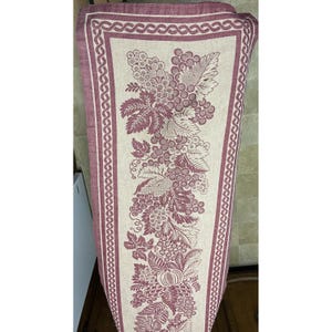 May include: A burgundy and cream table runner with a grapevine design. The runner features a repeating pattern of grapes and leaves.