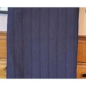 May include: A navy blue fabric with a textured, vertically ribbed pattern. The fabric appears to be a solid color, with a subtle sheen. The material is likely used for clothing or home decor.
