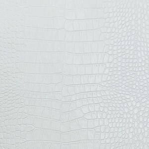 Pode incluir: Um close-up de uma superf&iacute;cie branca texturizada com um padr&atilde;o que se assemelha &agrave; pele de crocodilo ou jacar&eacute;. O padr&atilde;o consiste em formas retangulares e ovais, criando uma apar&ecirc;ncia de escamas. A superf&iacute;cie &eacute; uniformemente iluminada.