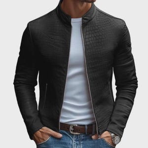 Pode incluir: Casaco de couro preto com um padr&atilde;o texturizado semelhante ao de um crocodilo. O casaco tem uma gola alta, um z&iacute;per prateado e dois bolsos laterais. A pessoa est&aacute; vestindo uma camiseta branca e jeans azuis.