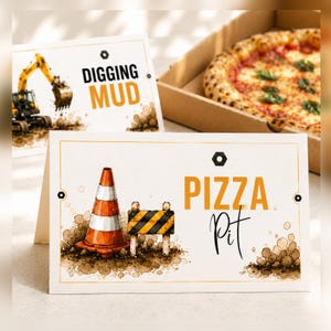 May include: Two greeting cards with construction-themed designs. One card says "Digging Mud" with an excavator illustration. The other says "Pizza Pit" with a traffic cone and barrier illustration. A pizza in a box is in the background.