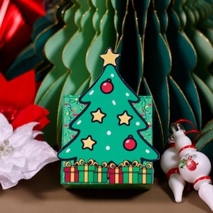 Könnte beinhalten: Eine grüne Weihnachtsbaum-Dekoration mit gelben Sternen und roten Kugeln. Der Baum steht auf einer Schachtel mit Geschenkillustrationen. Der Hintergrund zeigt grüne Papier-Weihnachtsbaumdekorationen und weiße und rote Weihnachtssternblumen.