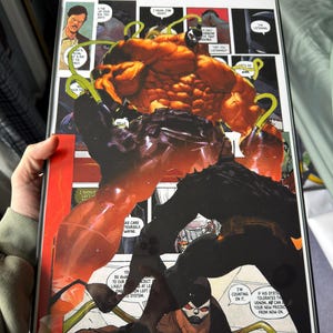 May include: Comic book art featuring a muscular, orange-toned figure with a black, shadowy figure. The artwork includes speech bubbles and text, with the word "HELLO" visible. The comic is framed in a black border.