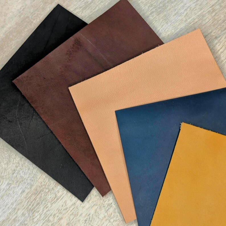 May include: A selection of leather swatches in shades of black, brown, tan, navy blue, and mustard yellow. The leather samples are fanned out, displaying the different textures and colours of the material. Ideal for craft projects or material selection.