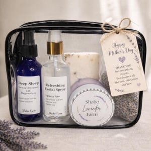 May include: A clear cosmetic bag filled with self-care products. Includes a blue spray bottle labeled "Deep Sleep Lavender Hydrosol", a clear spray bottle labeled "Refreshing Facial Spray", a bar of soap, a jar of cream, and a bag of lavender. A tag reads "Happy Mother's Day".