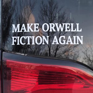 May include: A white decal on a car window reads "MAKE ORWELL FICTION AGAIN" in a bold, sans-serif font. The car's taillight is visible, with a red lens and a white car body. The background shows bare trees and snow.