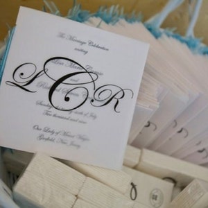 Può includere: Un cesto bianco pieno di programmi di cerimonia di matrimonio in carta bianca piegata. I programmi presentano le iniziali della coppia "L.R." in un carattere corsivo nero. Il testo del programma recita "The Marriage Celebration uniting Lisa Marie Ragonese and Richard Steven Jr. Sunday, the sixth of July, Two thousand and seven. Our Lady of Mount Virgin, Garfield, New Jersey."