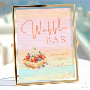 May include: A gold-framed sign featuring a pastel-colored wood grain background. The text reads Waffle Bar, Grab Waffles, Add Topping, and Bite & Enjoy. An illustration of a waffle topped with whipped cream, strawberries, and blueberries is included.