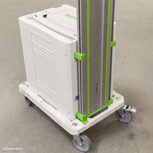 Puede incluir: Un maletín de almacenamiento blanco Festool y un riel guía vertical de aluminio con detalles en verde montados sobre una plataforma rodante blanca con cuatro ruedas giratorias. El riel guía tiene la etiqueta FS 1400/2 y la marca Festool.