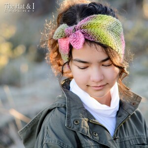 May include: A young person wearing a green, pink, and brown crocheted headband with a bow. The headband is tied in a knot at the top of the head. The person is wearing a green jacket and a white shirt.
