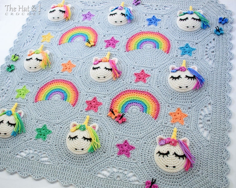 Puede incluir: Una manta de beb&eacute; de crochet con un fondo azul claro que presenta un patr&oacute;n repetitivo de arco&iacute;ris, estrellas y aplicaciones de unicornio. The Hat & I Crochet est&aacute; impreso en la esquina superior izquierda.