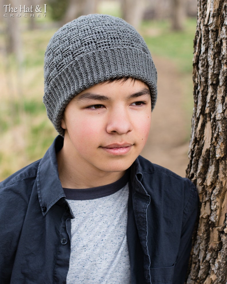 May include: A grey crocheted beanie with a textured stitch pattern. The beanie is being worn by a person with dark hair and brown eyes.