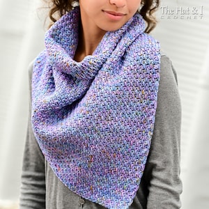 Puede incluir: Una bufanda triangular de ganchillo con un patrón de puntos texturizados en tonos variados de lavanda, azul claro y morado. La bufanda está colocada alrededor del cuello y los hombros, mostrando una apariencia densa y tejida con sutiles motas de color.