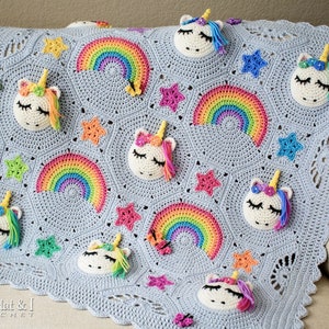 Puede incluir: Una manta de beb&eacute; de crochet con un fondo azul claro que presenta un arco&iacute;ris, estrellas y aplicaciones de unicornio. La manta tiene un borde festoneado y est&aacute; hecha con un punto texturizado.
