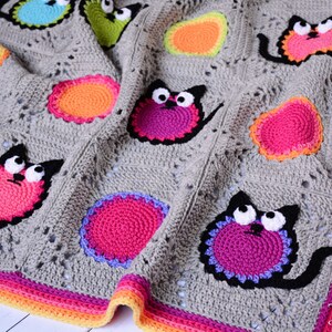 May include: A gray crochet baby blanket with a colorful border and appliqued cats. The cats are made with different colored yarn and have black eyes and mouths.
