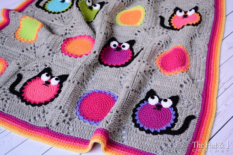 May include: A gray crochet baby blanket with a colorful border and appliqued cats. The cats are made with different colored yarn and have black eyes and mouths.