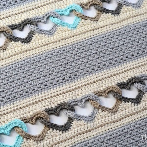 May include: A crocheted blanket with a striped pattern in shades of gray and beige. The blanket features a repeating heart design in turquoise, brown, and gray.