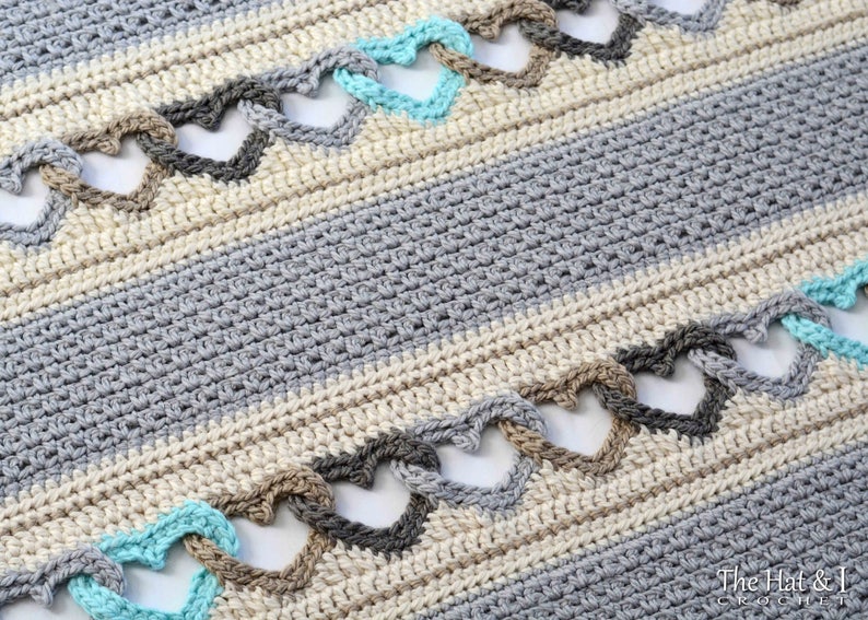 May include: A crocheted blanket with a striped pattern in shades of gray and beige. The blanket features a repeating heart design in turquoise, brown, and gray.