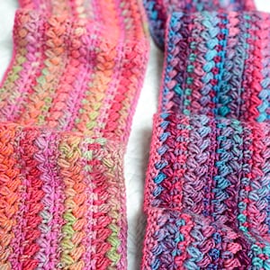 Pu&ograve; includere: Due sciarpe all'uncinetto in filato multicolore con sfumature di rosa, blu e verde. Le sciarpe sono realizzate con un punto a trama.