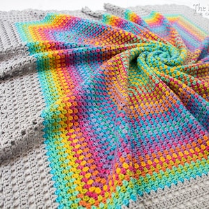 May include: A crocheted blanket with a rainbow pattern in the center and a gray crocheted border. The blanket is made with a variety of colors including pink, blue, green, yellow, and orange. The blanket is folded in a spiral shape. The text 'The Hat & I CROCHET' is visible in the upper right corner of the image.