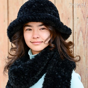 May include: A young person wearing a black fuzzy hat and matching scarf. The hat has a wide brim and the scarf is long and wraps around the neck.