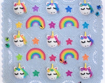 May include: A crocheted baby blanket with a light blue background featuring a repeating pattern of rainbows, stars, and unicorn faces. The blanket has a scalloped edge.