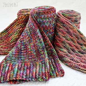 May include: Three colorful, hand-crocheted scarves in shades of red, purple, green, and orange. Two scarves are rolled up, while the third is partially unfolded, displaying the intricate stitch pattern. The scarves are made of a soft, textured yarn.