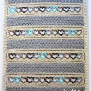 May include: A crocheted baby blanket with a striped pattern in beige, gray, and brown. The blanket features a repeating heart design with a turquoise accent.