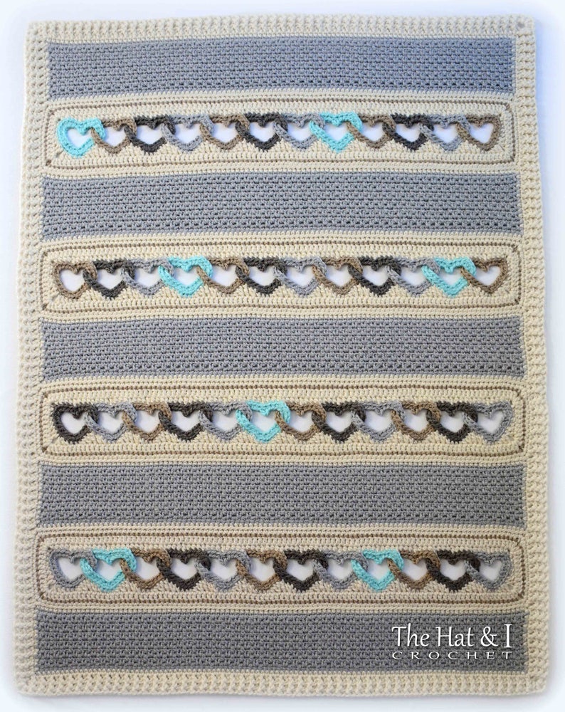 May include: A crocheted baby blanket with a striped pattern in beige, gray, and brown. The blanket features a repeating heart design with a turquoise accent.