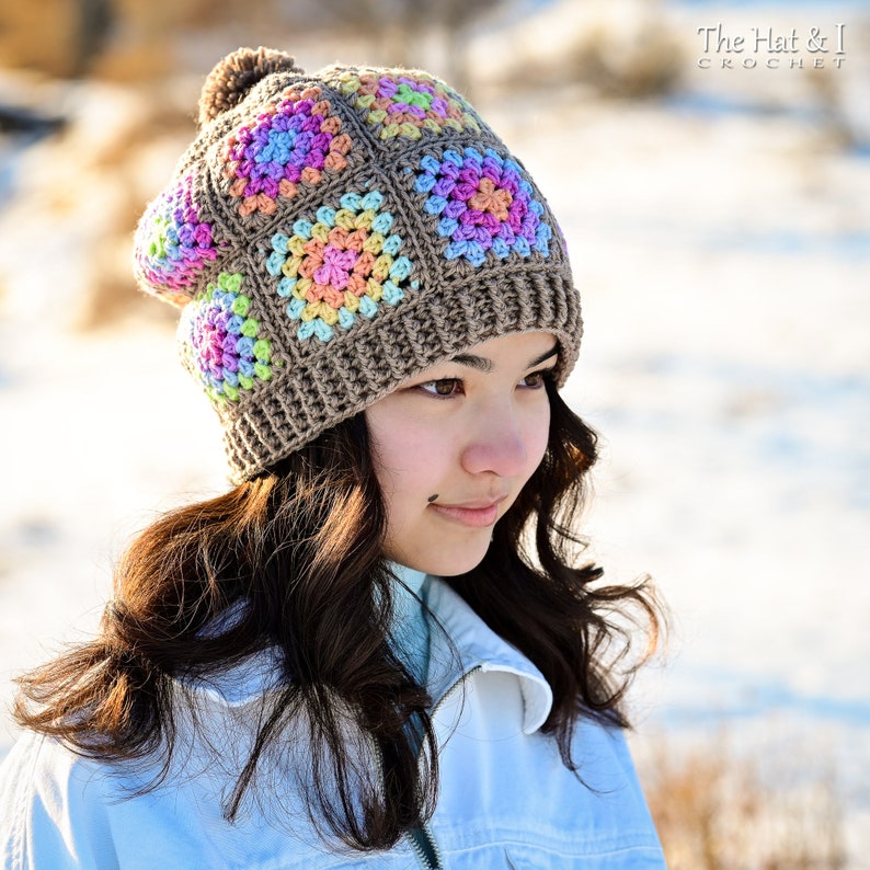 Puede incluir: Un gorro de ganchillo hecho a mano con un dise&ntilde;o de cuadrados de la abuela colorido. El gorro presenta cuadrados en tonos de rosa, azul, amarillo y verde, sobre un fondo marr&oacute;n. Un pomp&oacute;n marr&oacute;n se encuentra en la parte superior del gorro. El texto "The Hat & I Crochet" es visible.