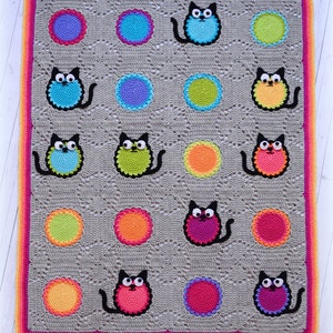 May include: A crocheted blanket with a gray background and colorful circles and cats. The blanket has a pink, orange, and yellow border.