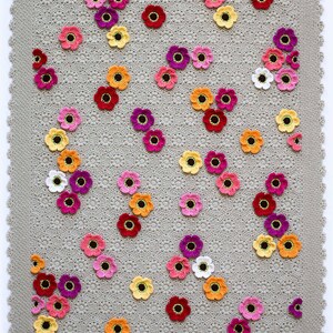 May include: A crocheted blanket with a gray background and a pattern of colorful flowers. The flowers are in shades of pink, red, orange, yellow, and white.