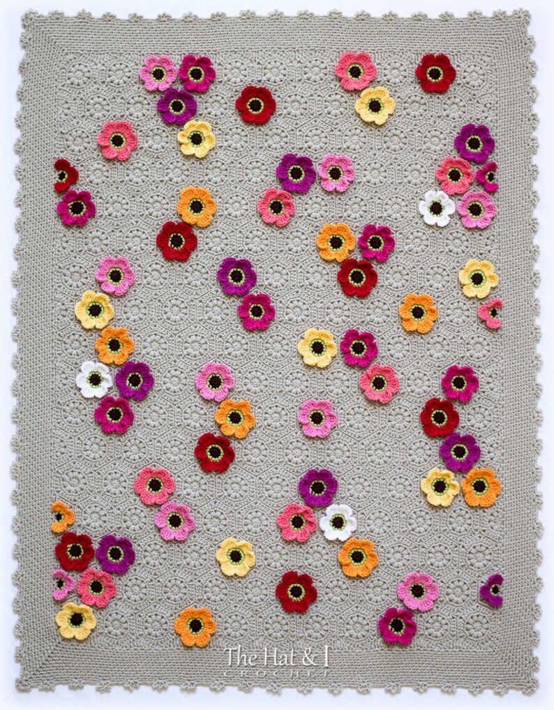 May include: A crocheted blanket with a gray background and a pattern of colorful flowers. The flowers are in shades of pink, red, orange, yellow, and white.