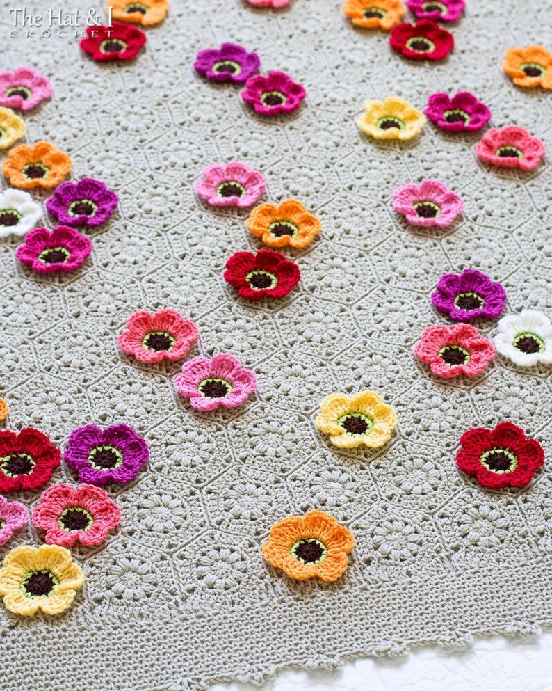 May include: A crocheted blanket with a gray background and colorful flower appliques. The flowers are in various shades of pink, red, orange, and yellow.