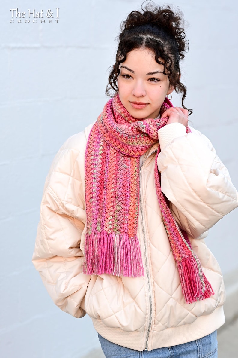 Pu&ograve; includere: Una sciarpa all'uncinetto rosa e arancione con frange. La sciarpa &egrave; indossata da una persona che indossa una giacca trapuntata color crema.