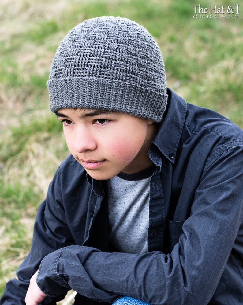 May include: A grey crocheted beanie with a textured woven pattern. The beanie is being worn by a person with dark hair and brown eyes.