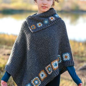 May include: A gray crochet poncho with a cowl neck and floral border. The poncho features a repeating pattern of square floral motifs in shades of orange, blue, and white. The text "The Hat & I Crochet" is at the top.