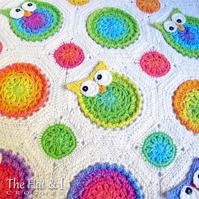 May include: A white crochet baby blanket with colorful owl and circle motifs. The blanket features a repeating pattern of owls and circles in shades of green, blue, pink, orange, and yellow.