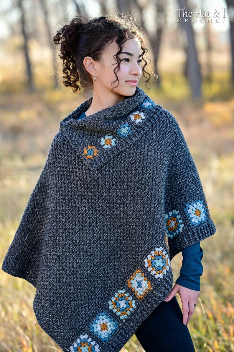 May include: A dark gray crochet poncho with a cowl neck and floral square accents in blue, orange, and white. The poncho has a textured stitch pattern and is worn by a person. The text "The Hat & I Crochet" is visible in the upper right corner.