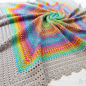 May include: A crocheted blanket with a gray border and a rainbow colored center. The blanket is made with a textured stitch and has a scalloped edge. The text 'The Hat & I CROCHET' is visible in the bottom right corner of the image.