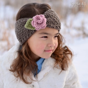 May include: A brown crocheted headband with a pink flower and green leaf embellishment. The headband is worn by a person wearing a white coat. The text "The Hat & I Crochet" is in the upper right corner.