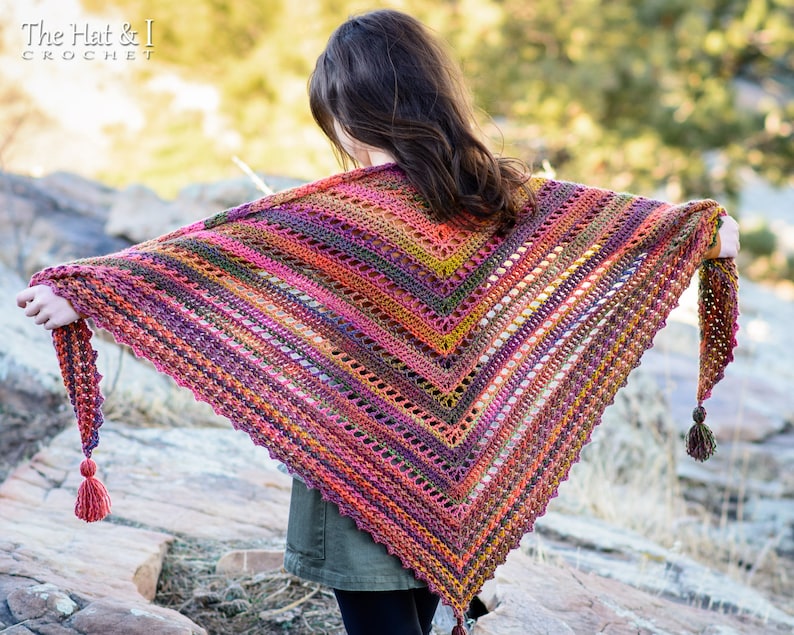 Puede incluir: Un chal de ganchillo colorido con un patr&oacute;n geom&eacute;trico y borlas. El chal est&aacute; hecho con una variedad de tonos de rojo, naranja, amarillo, verde y morado.