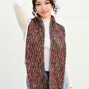 May include: A multi-colored knitted scarf and matching headband. The scarf is long and features a textured pattern with hues of red, green, and purple. The headband has a similar design. The text "The Hat & I Crochet" is visible in the upper right corner.