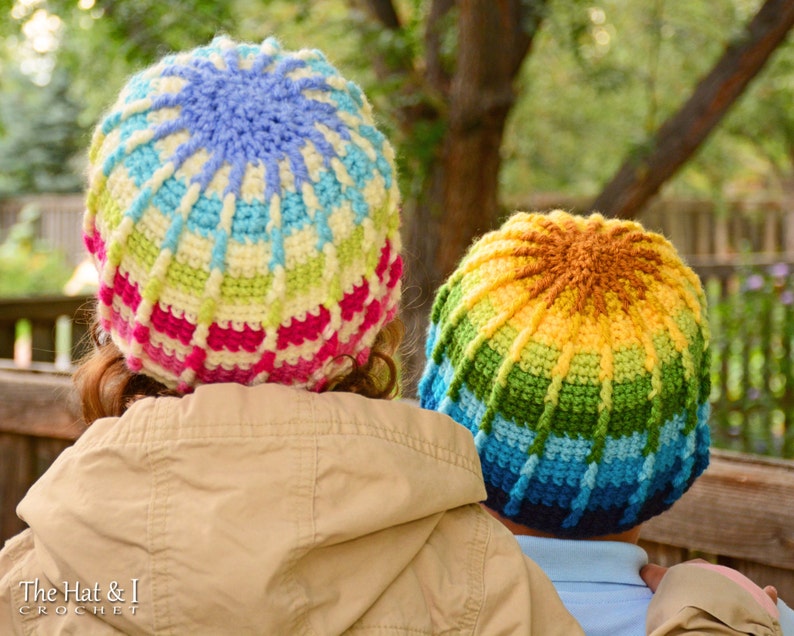 Pu&ograve; includere: Due bambini indossano cappelli all'uncinetto colorati. I cappelli sono realizzati con un arcobaleno di colori, tra cui rosso, arancione, giallo, verde, blu e viola. I cappelli sono all'uncinetto in un motivo circolare, con un design a stella nella parte superiore.