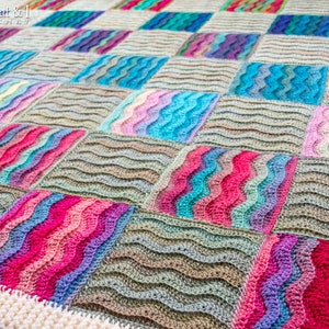Pode incluir: Uma manta de croch&ecirc; colorida com um padr&atilde;o ondulado. A manta &eacute; composta por quadrados de diferentes cores, incluindo rosa, azul, verde e marrom. A manta &eacute; feita de croch&ecirc; com uma borda branca.