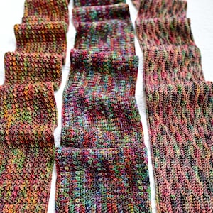 May include: Several hand-crocheted scarves in various patterns and colors are displayed on a white surface. The scarves feature a mix of vibrant hues, including red, green, purple, and orange. The image showcases the texture and detail of the handmade items.
