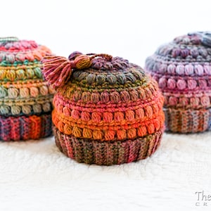 May include: Three crocheted hats with colorful yarn and pom-poms. The hats are made with a textured stitch and have a variety of colors, including pink, purple, blue, green, and orange.