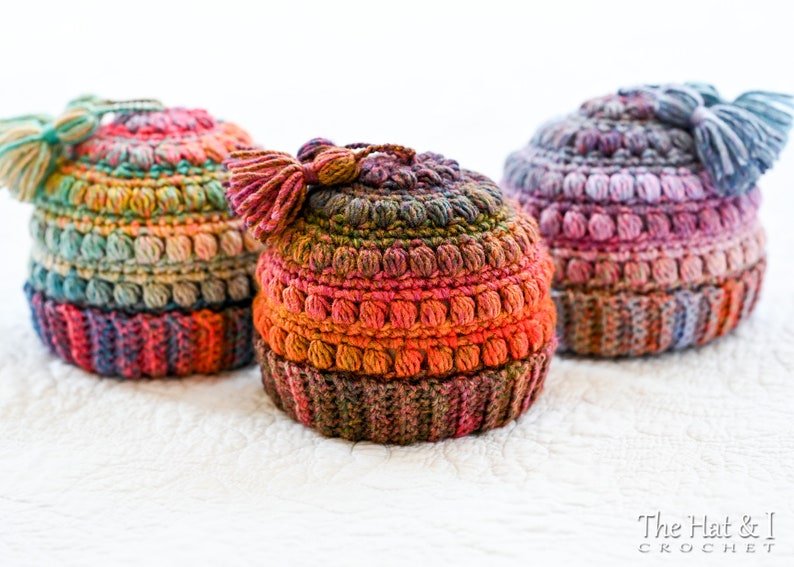 May include: Three crocheted hats with colorful yarn and pom-poms. The hats are made with a textured stitch and have a variety of colors, including pink, purple, blue, green, and orange.